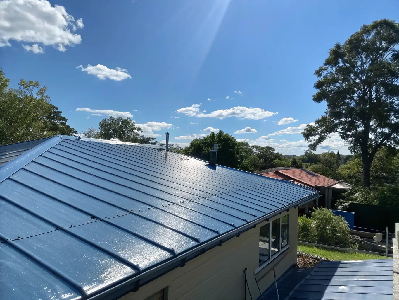A wide shot of a residential roof being cleaned and treated with a protective coating. The roof should appear clean and well-maintained, with a visible difference between the treated and untreated areas. The surrounding environment is lush and green, indicating a healthy and well-cared-for property.